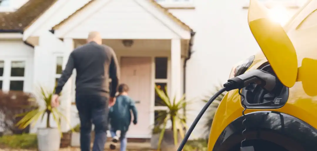 An electric vehicle charing with a father and son walking into their home